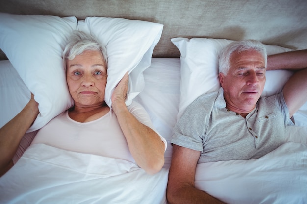 Esposa bloqueando las orejas con almohada mientras el esposo ronca en la cama