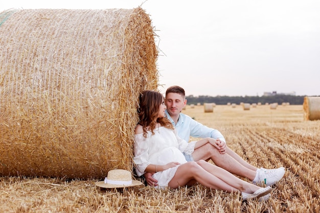 Una esposa y un esposo embarazadas descansan en un campo de trigo segado en un picnic