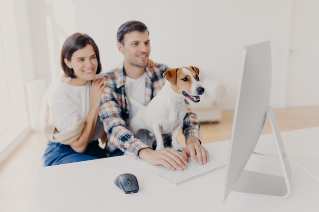 La esposa y el esposo jóvenes positivos leen la publicación en línea, se sientan frente a la computadora, miran la película favorita o la película junto con la mascota. Se centran en los animales. La pareja pasa tiempo con las tecnologías modernas.