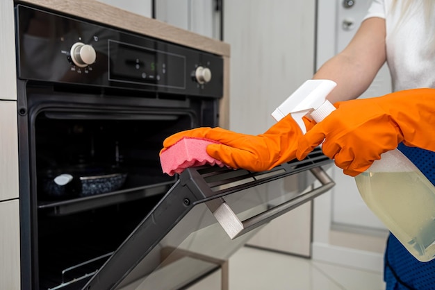 Esposa en guante naranja limpiando la puerta del horno en su concepto de desinfectante de tareas domésticas de cocina