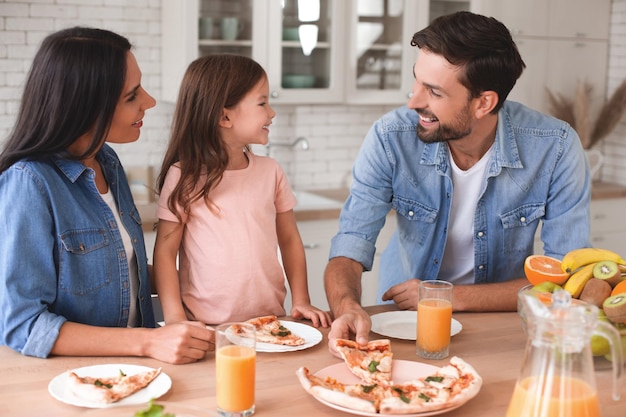 Esposa marido e filha comendo pizza para almoçar em casa