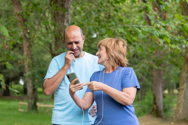 Esposa mostrando algo en el teléfono inteligente a su esposo después de hacer ejercicio en la montaña en la naturaleza