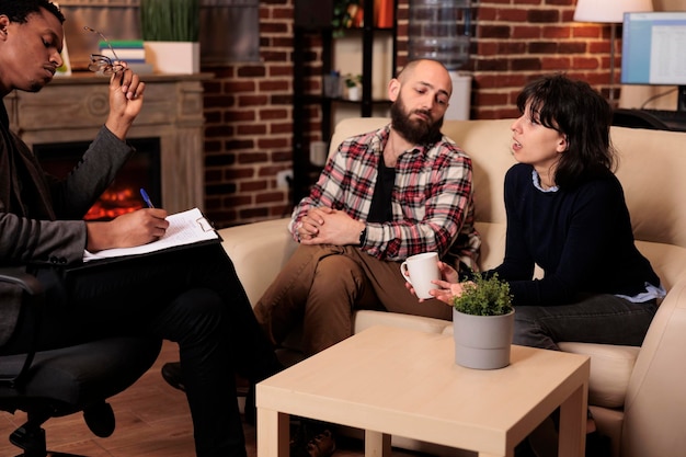 Esposa preocupada conversando com conselheiro sobre problemas conjugais, participando de terapia de casal com marido e especialista. Tentando resolver conflitos de relacionamento com apoio profissional.