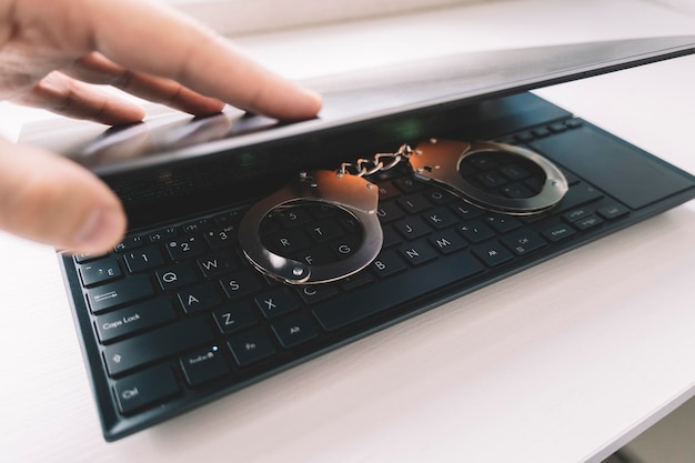 Esposas de metal en un teclado negro Esposas en el primer plano de la computadora portátil Concepto de crimen de hacker cibernético