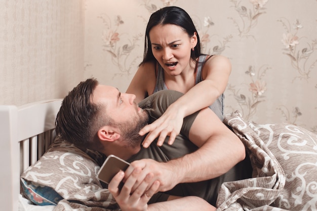 El esposo mira el teléfono de la esposa en la cama