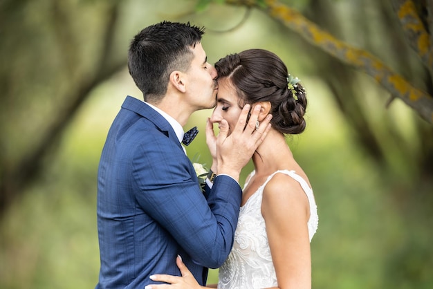 El esposo recién casado sostiene la cabeza de su esposa en sus palmas y la besa en la frente