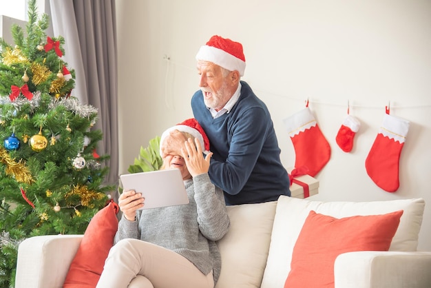 El esposo de Senier le da una caja de regalo a su esposa mientras se sienta en el sofá y usa un sombrero de Papá Noel