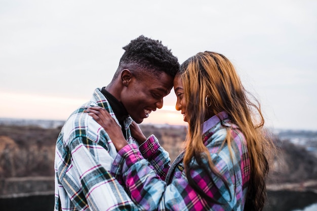 El esposo sostiene a su joven esposa en sus brazos detrás de un hermoso cielo Pareja elegante con camisas a cuadros enamorados juntos