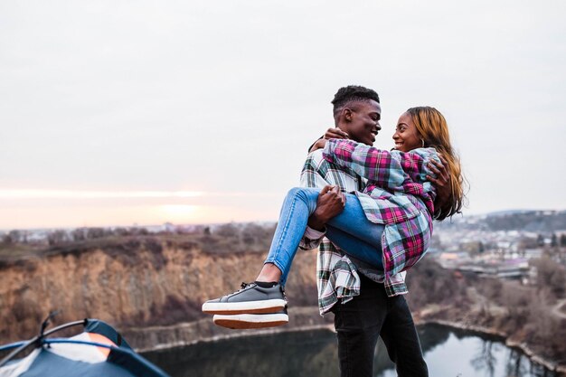 El esposo sostiene a su joven esposa en sus brazos detrás de un hermoso cielo Pareja elegante con camisas a cuadros enamorados juntos