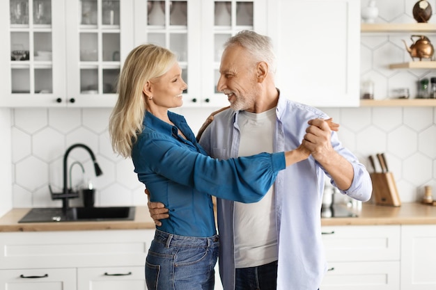 Esposos felices amando a marido y mujer mayores bailando en el interior de la cocina