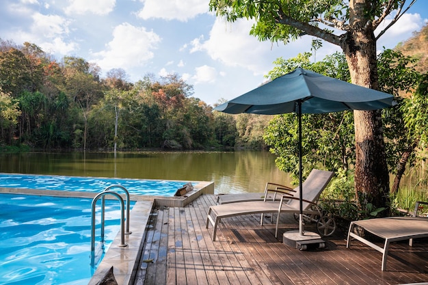 Espreguiçadeira com guarda-sol no terraço à beira da piscina entre a floresta tropical e o lago no resort Conceito de verão e férias