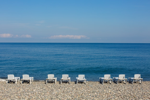 Espreguiçadeiras brancas na praia perto do mar no seixo