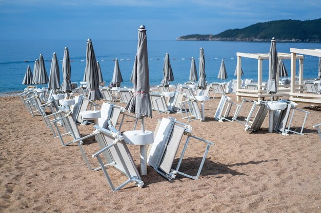 Espreguiçadeiras brancas vazias sem pessoas sob o guarda-sol na praia de seixos à beira-mar