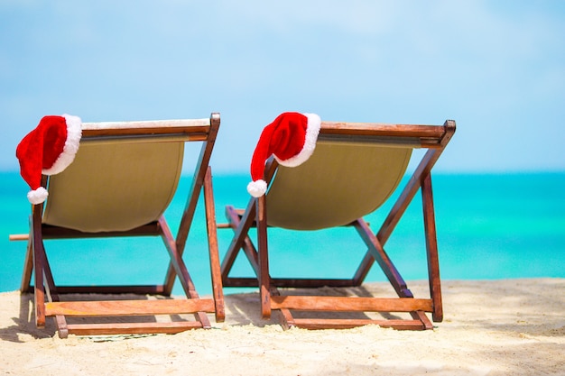 Espreguiçadeiras com chapéu de papai noel na bela praia tropical com areia branca e água azul-turquesa.