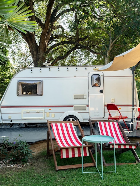 Espreguiçadeiras vazias na praia e cadeiras dobráveis com mesa em frente ao parque de estacionamento de caravanas em estilo vertical de jardim Relaxamento acampar e dormir no trailer de autocaravana Conceito de viagem de férias em família