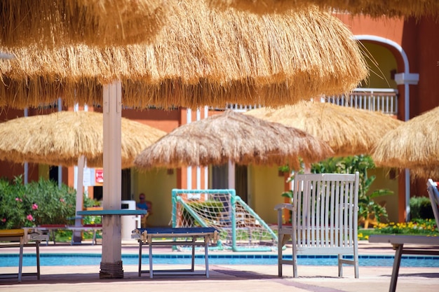 Espreguiçadeiras vazias sob guarda-chuvas de palha no lado da piscina no resort tropical Férias de verão e conceito de fuga