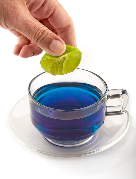 Espremer manualmente o suco de limão para o chá de ervilha borboleta transformará a água roxa chá de ervilha borboleta isolado no chá de ervas de fundo branco