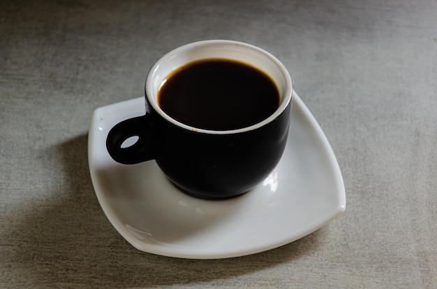 Espresso caliente en una taza negra sobre un fondo gris