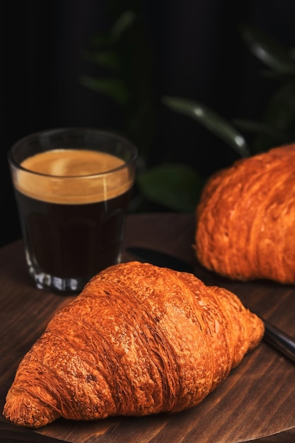 Espresso e croissants no café da manhã em uma mesa de madeira em um café Café da manhã francês Foco seletivo vertical em um croissant