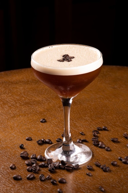 Espresso martini coquetel em copo servido sob suporte de borracha com grãos de café derramados na mesa de madeira vista de perto