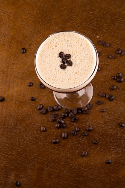 Espresso martini coquetel em copo servido sob suporte de borracha com grãos de café derramados na mesa de madeira