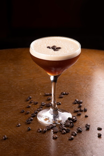 Espresso martini coquetel em copo servido sob suporte de borracha com grãos de café derramados na mesa em retrato