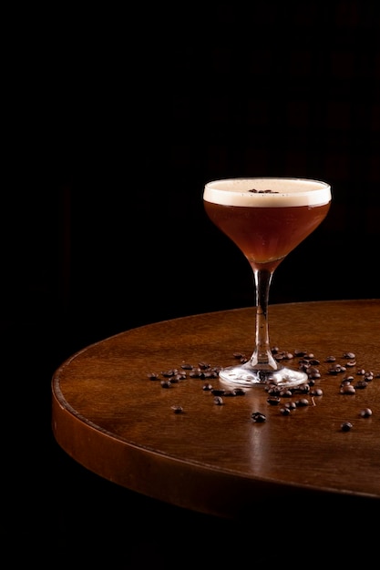 Espresso martini coquetel em copo servido sob suporte de borracha com grãos de café derramados no canto da mesa bistrô