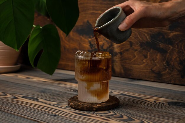 Espresso Tonic kaltes Erfrischungsgetränk in der Zubereitung Kaffee in ein Glas mit Eiswürfeln und Sodawasser auf Holzhintergrund gießen