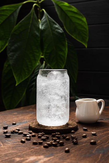 Espresso tônico em preparação Um copo alto cheio de cubos de gelo tônico água com gás grãos de café jarro de leite fundo de madeira