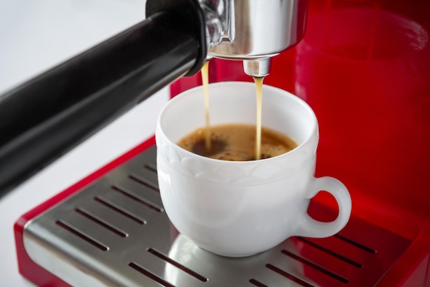 Espressokaffee, der zu Hause aus der Maschine in eine weiße Tasse gegossen wird