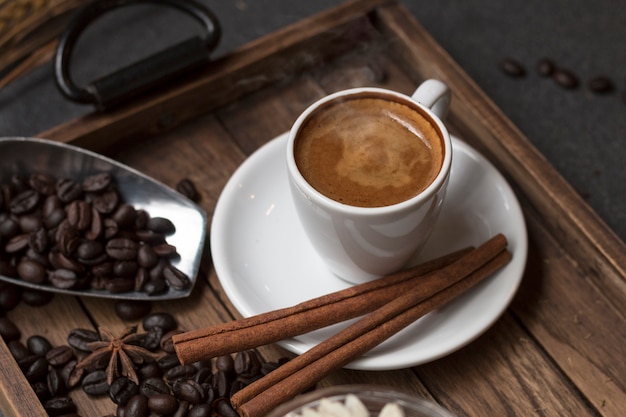 Foto espressotasse, kaffeebohne, zimt und trockenblumenglas auf hölzernem behälter.