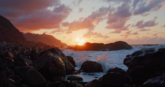 Espuma de água do mar branca espalha-se sobre a escarpada costa de rocha preta em Tenerife ao pôr-do-sol Imagem cinematográfica de ondas oceânicas batendo na costa vulcânica das Ilhas Canárias na hora dourada