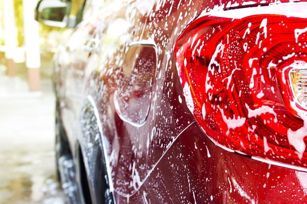 Espuma de lavagem de carro em carro vermelho. Lavagem de carros e limpeza de fundo.
