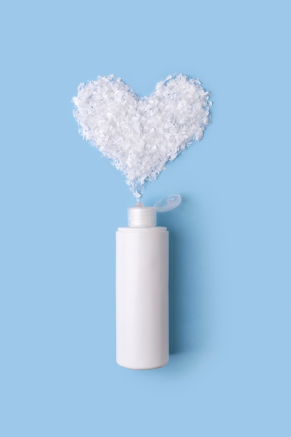 Espuma de limpeza em uma garrafa com coração de neve na mesa azul