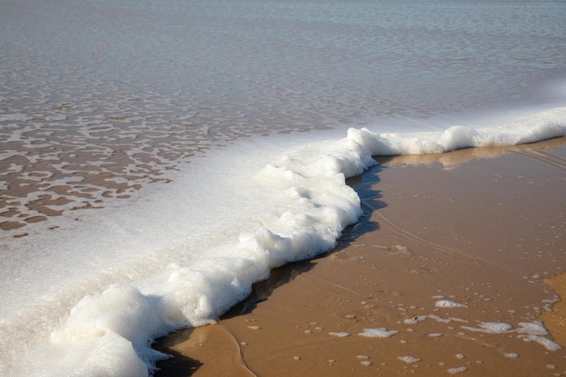 Espuma do mar na costa da praia de areia onda oceânica chegando na maré baixa de vista arenosa