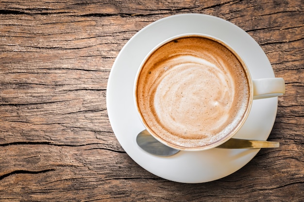 Espuma espumosa de café com leite quente cappuccino em copo branco na mesa de madeira velha