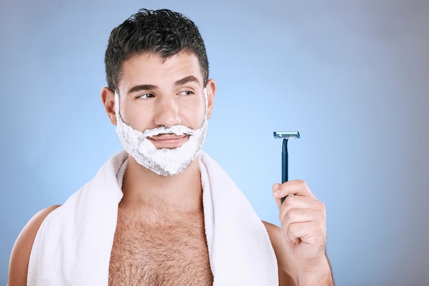 Espuma facial en la barba y el hombre con una navaja en la toalla de mano y colocación de productos y simulacros en el estudio