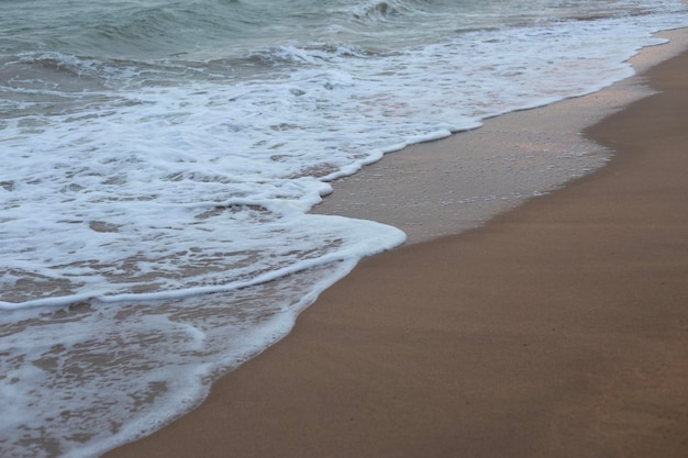 La espuma de las olas del mar en la playa de arena cierra el fondo