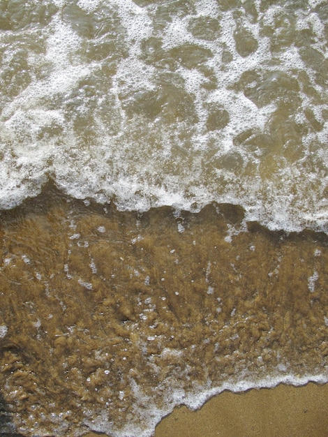 Espuma en una playa de arena, olas en el océano