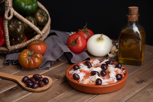 Foto esqueixada en cazuela de barro y cuchara de madera con algunas aceitunas negras.