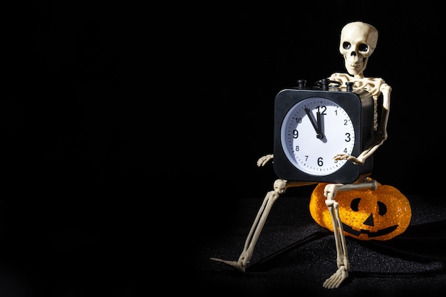 Un esqueleto sentado en una lámpara en forma de letra con una sonrisa y sosteniendo un despertador sobre un fondo negro Hora de los Muertos