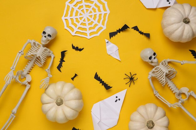 Esqueletos y calabazas de decoración hecha a mano de Halloween sobre fondo amarillo Vista plana superior