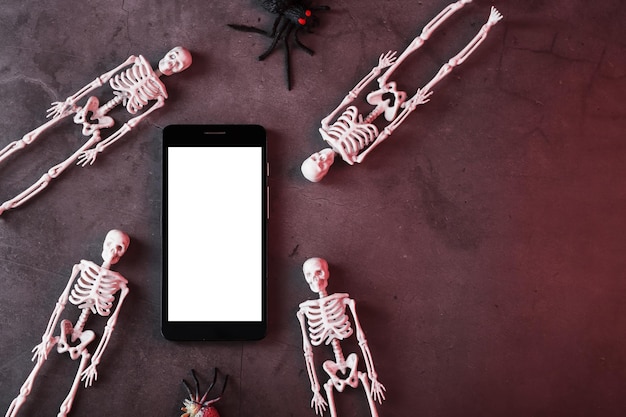 Los esqueletos decorativos se encuentran cerca del teléfono inteligente sobre un fondo oscuro. Decoración de Halloween, Vista superior, Espacio libre