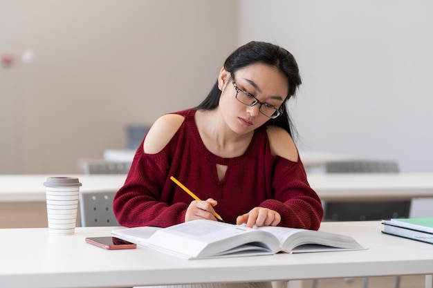 Esquema de escritura de niña asiática inteligente mientras se prepara para el examen en la sala de lectura o en el aula