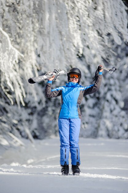 Esquiador em pé, aproveitando o dia ensolarado contra árvores cobertas de neve no fundo