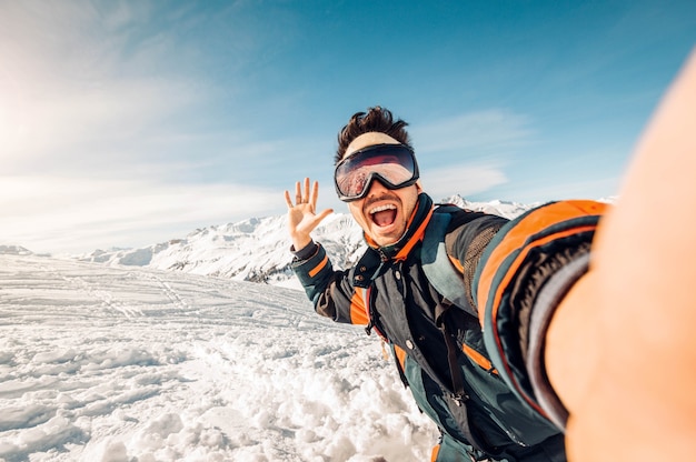 Esquiador feliz tirando uma selfie nas montanhas Jovem se divertindo esquiando ladeira abaixo na floresta de inverno