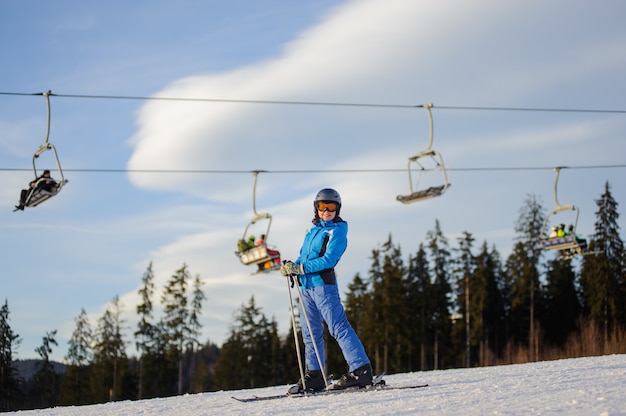 Esquiador feminino contra ski-lift e floresta em um dia ensolarado