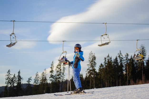 Esquiador feminino contra ski-lift e floresta em um dia ensolarado