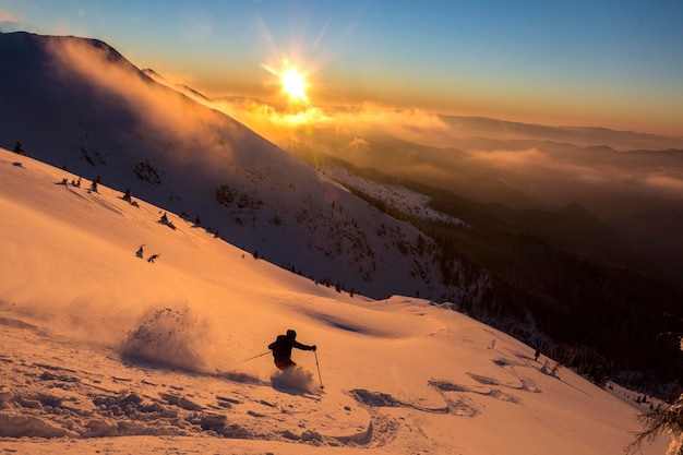 Esquiador freeride em belas montanhas nevadas cobertas com um pôr do sol laranja céu nublado Adrenalina aventuras de inverno ao ar livre