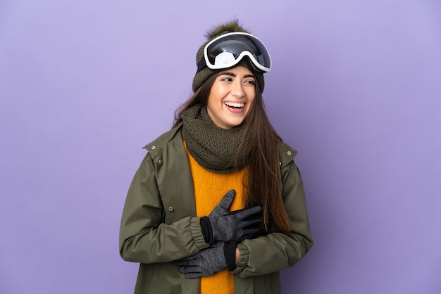 Esquiadora caucasiana com óculos de snowboard isolados no fundo roxo e sorrindo muito